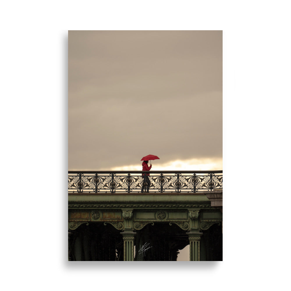 Photographie d'une femme traversant un pont parisien avec un parapluie rouge vif sur fond de paysage pluvieux.