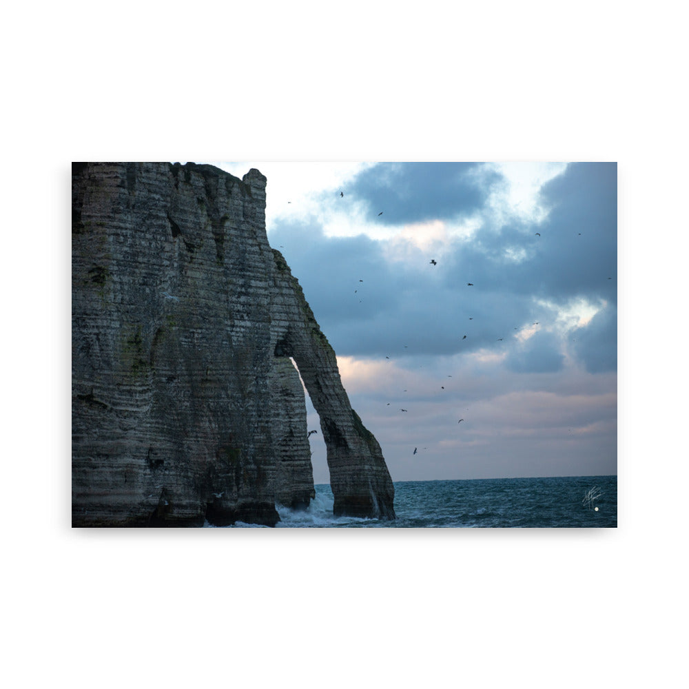 Vue panoramique des falaises d'Étretat avec des vagues s'écrasant puissamment sur la côte, sous un ciel nuageux où les mouettes virevoltent, incarnant la beauté sauvage de la Normandie.
