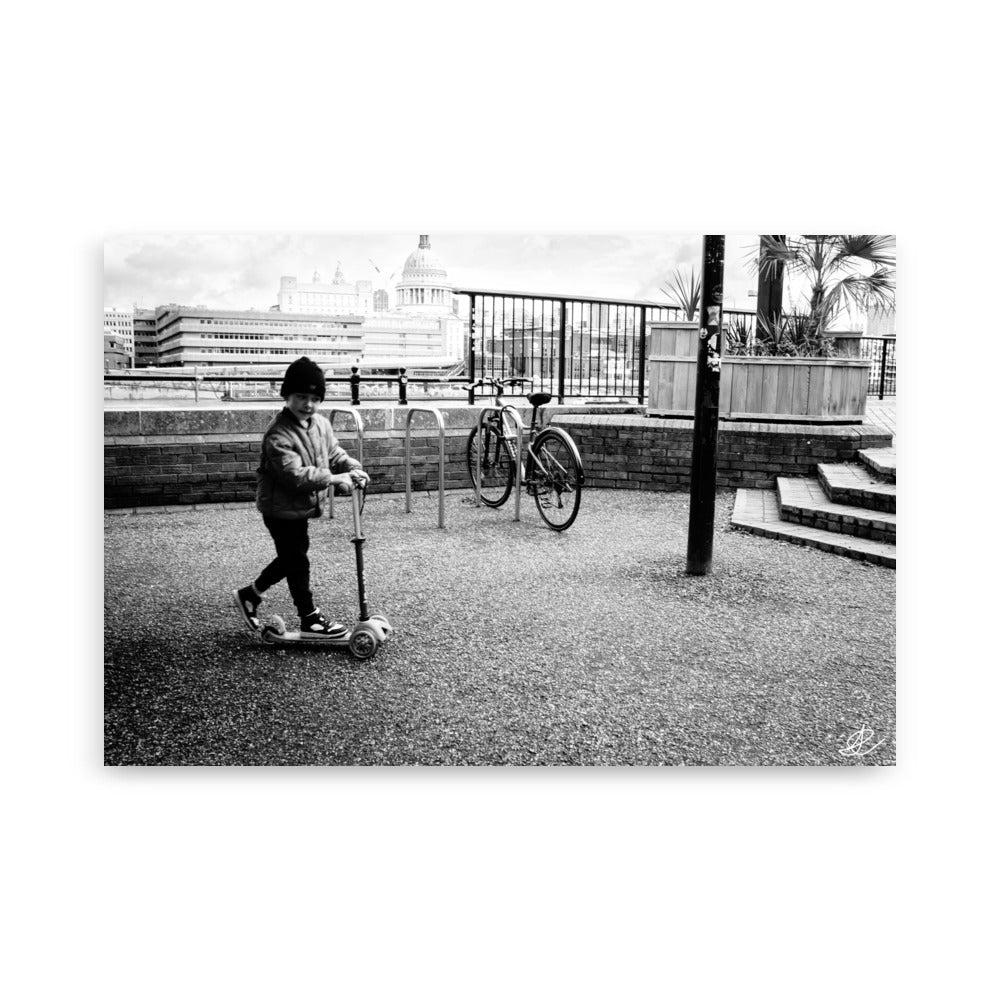 Photographie noir et blanc 'Trottinette' par Ilan Shoham, représentant un enfant joyeux trottinant sur les pavés de Londres, symbolisant l'innocence et la liberté