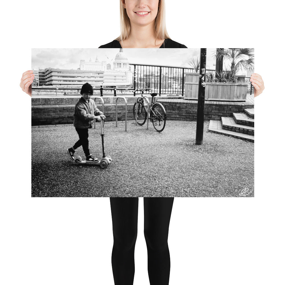 Photographie noir et blanc 'Trottinette' par Ilan Shoham, représentant un enfant joyeux trottinant sur les pavés de Londres, symbolisant l'innocence et la liberté
