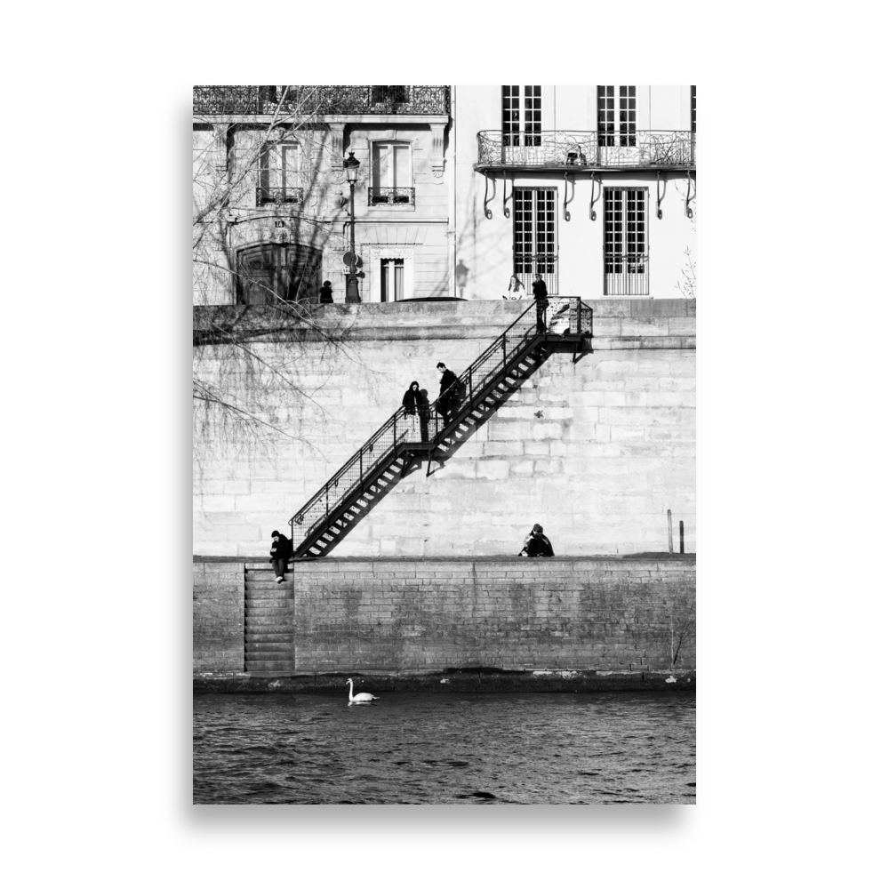 Photographie noir et blanc de personnes installées tranquillement sur les quais à Paris, encadrées par deux escaliers symétriques.