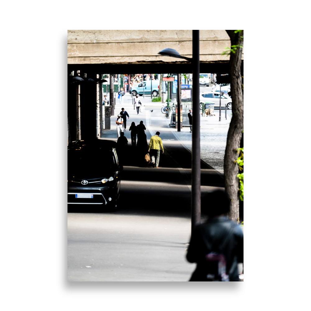 Un homme en veste verte kaki sous un pont ensoleillé.