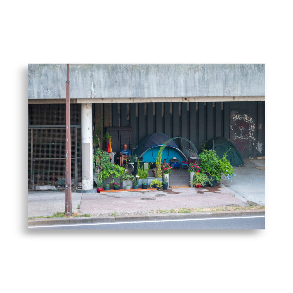 Photographie 'Maison de SDF' montrant une habitation improvisée de sans-abri à Paris, nichée à l'ombre d'un parking ancien près de la Seine.