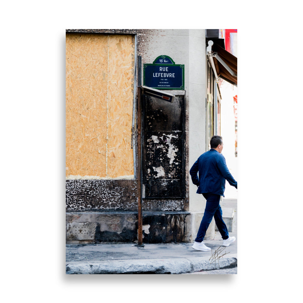 Photographie de la "Rue Lefebvre" après un incendie, montrant des traces de suie, un panneau de sens interdit plié et un passant.