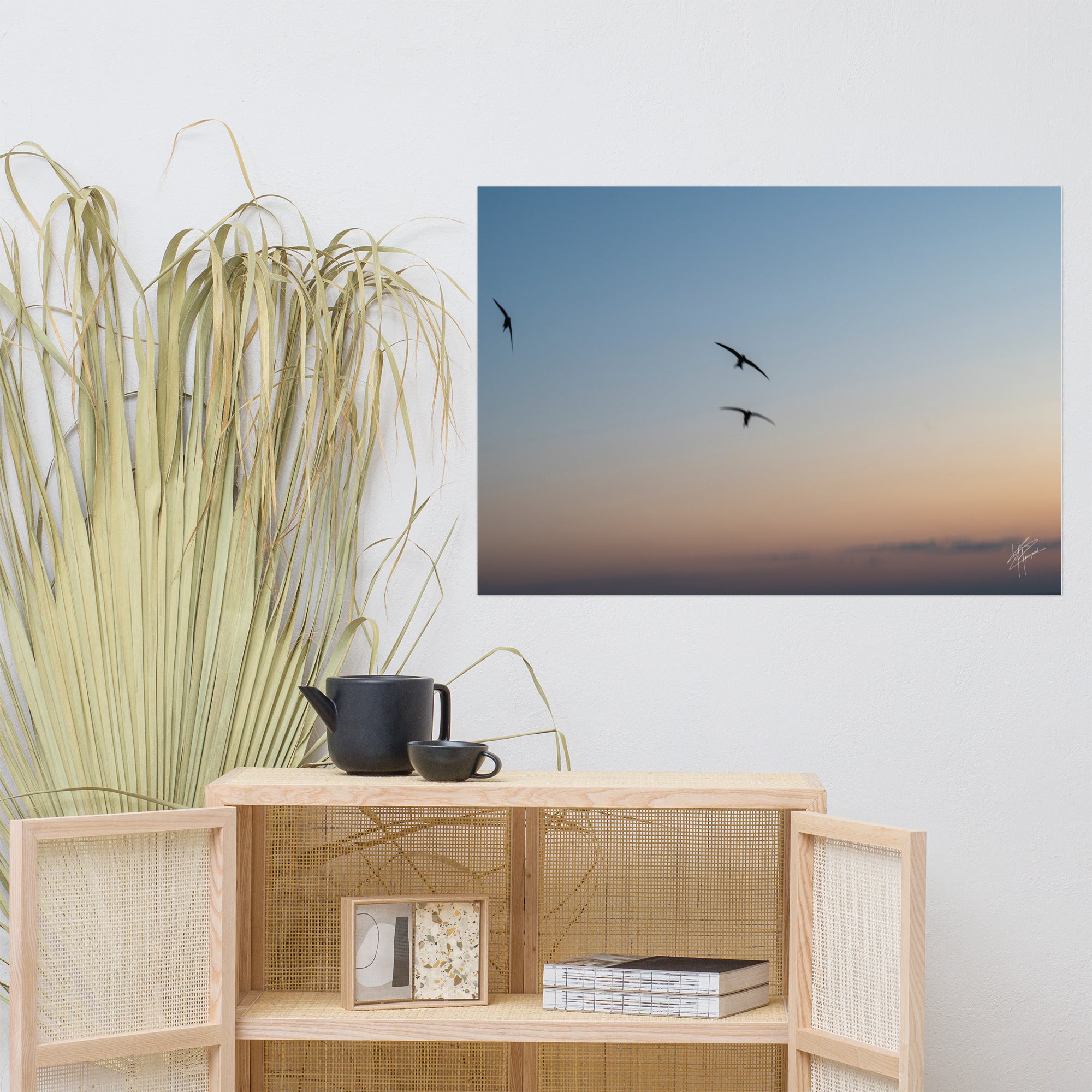 Trois oiseaux volant dans un ciel aux teintes de bleu, orange et jaune.