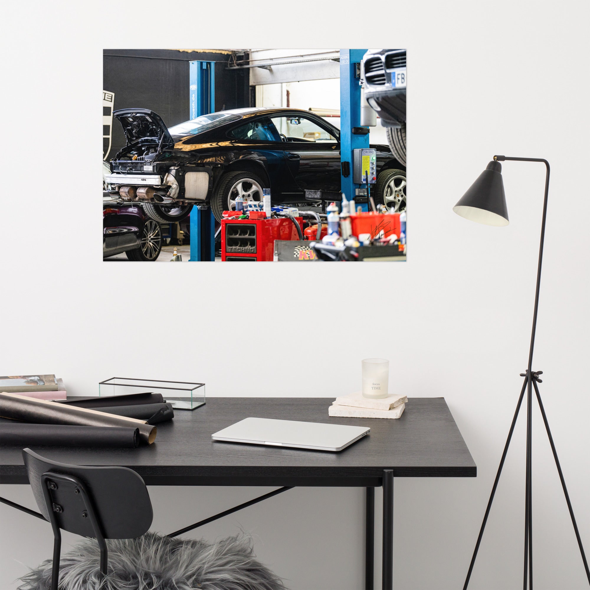 Photographie en noir et blanc d'une Porsche 911 sur un pont de révision, flanquée d'un Porsche Cayenne et d'un Porsche Macan dans un garage.