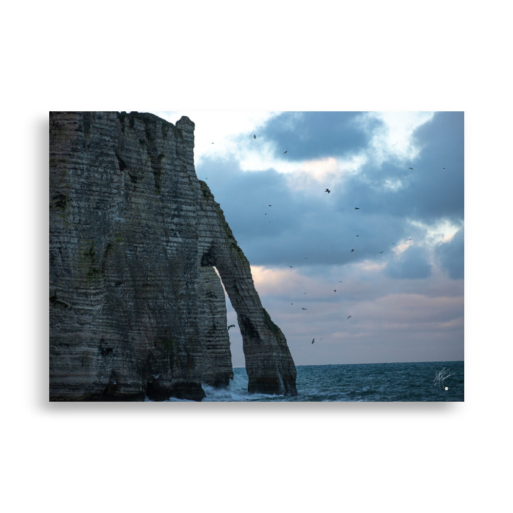 Vue panoramique des falaises d'Étretat avec des vagues s'écrasant puissamment sur la côte, sous un ciel nuageux où les mouettes virevoltent, incarnant la beauté sauvage de la Normandie.