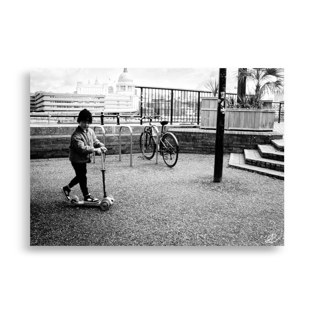 Photographie noir et blanc 'Trottinette' par Ilan Shoham, représentant un enfant joyeux trottinant sur les pavés de Londres, symbolisant l'innocence et la liberté