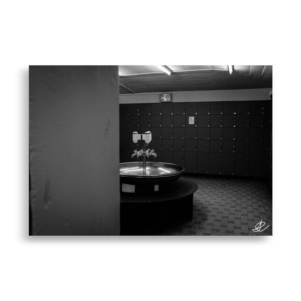 Photographie en noir et blanc d'un vestiaire vide, capturée par Ilan Shoham, offrant une vue discrète et intime, avec une vasque ronde et plusieurs robinets au centre.