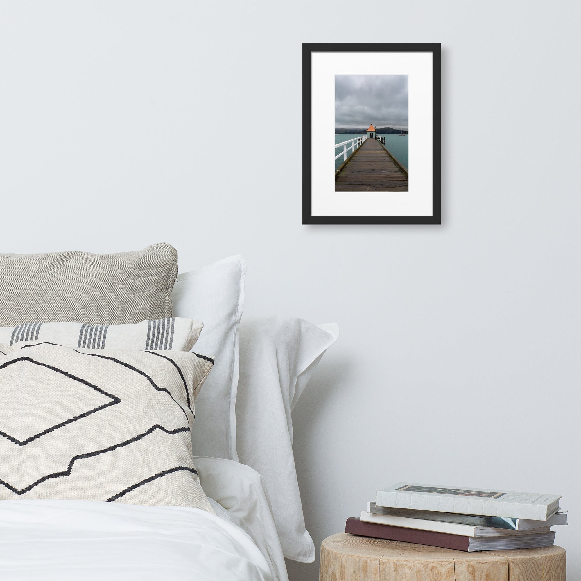 Photographie 'Akaroa NZ' de Charles Coley, offrant une vue sereine sur un lac néo-zélandais avec un petit abri au bout d'un ponton rustique, contrastant délicatement avec un arrière-plan de montagnes majestueuses et un ciel nuageux, ajoutant une dimension de tranquillité et d'évasion à votre espace.