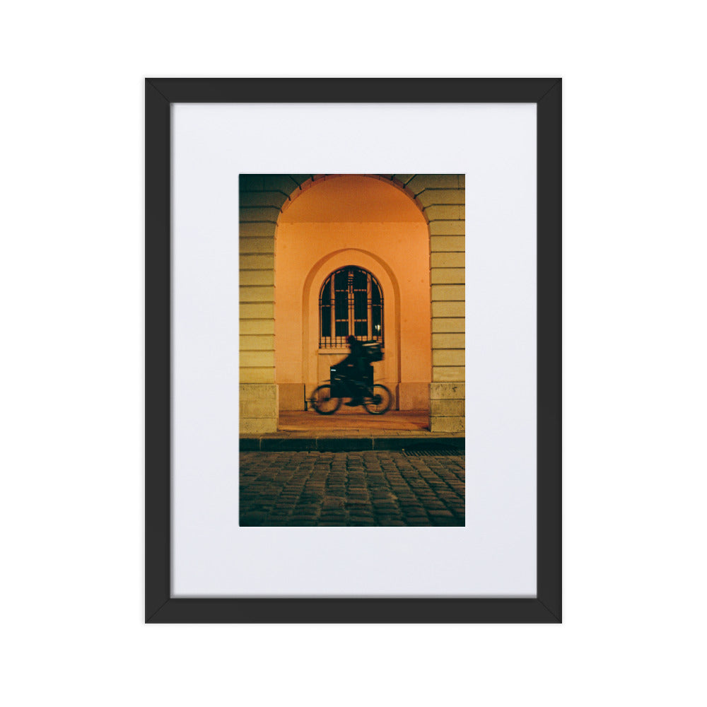 Photographie artistique 'Livraison à Toute Vitesse' par Benjamin Peccard, illustrant un moment urbain éphémère avec un livreur à vélo dans un flou de mouvement, traversant une scène de rue pittoresque éclairée d'une lueur orangée, un choix poétique et vibrant pour la décoration murale.