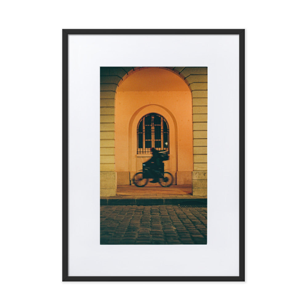Photographie artistique 'Livraison à Toute Vitesse' par Benjamin Peccard, illustrant un moment urbain éphémère avec un livreur à vélo dans un flou de mouvement, traversant une scène de rue pittoresque éclairée d'une lueur orangée, un choix poétique et vibrant pour la décoration murale.