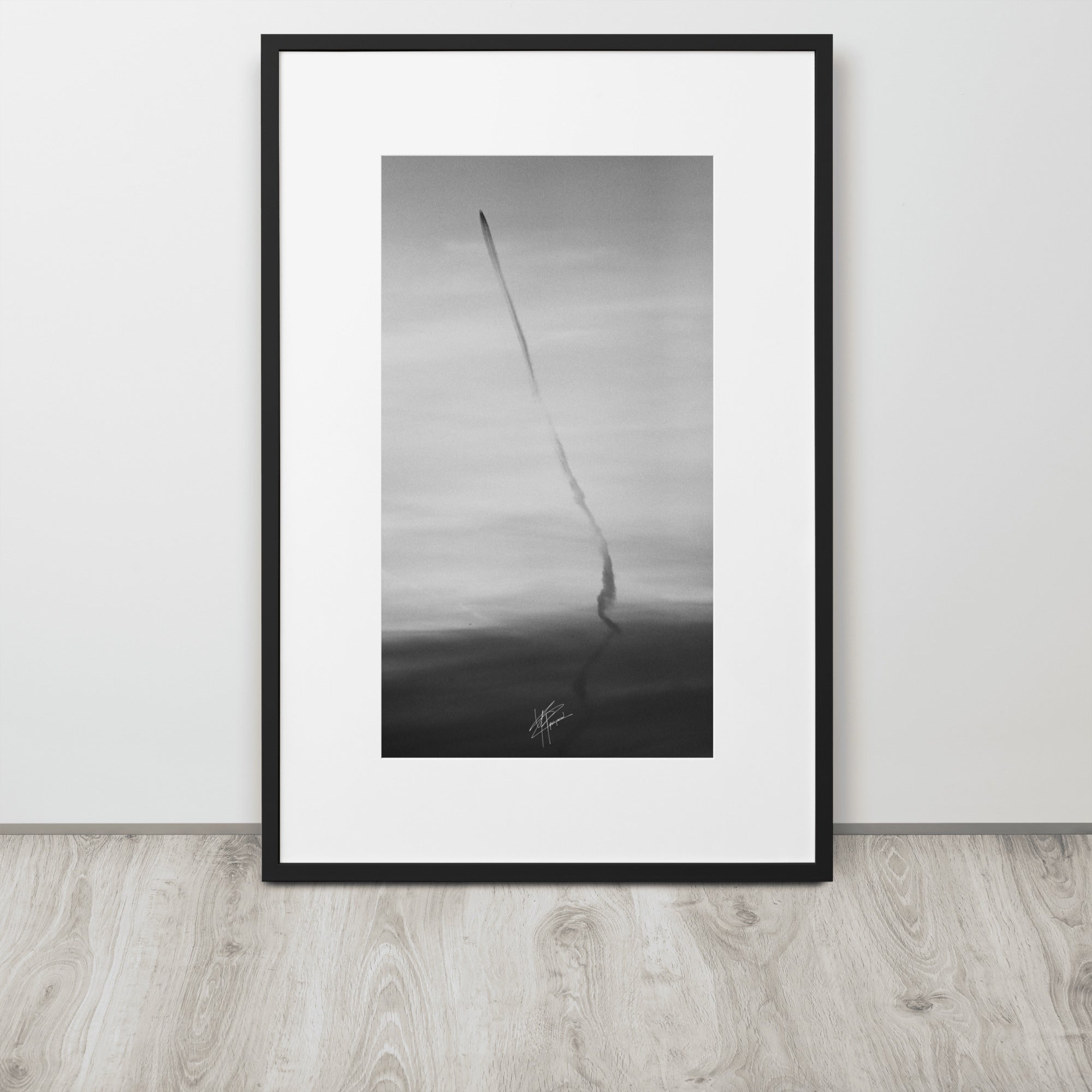 Photographie en noir et blanc du ciel avec des traces d'avions formant une longue ligne noire, encadrée d'un cadre en bois d'ayous blanc.