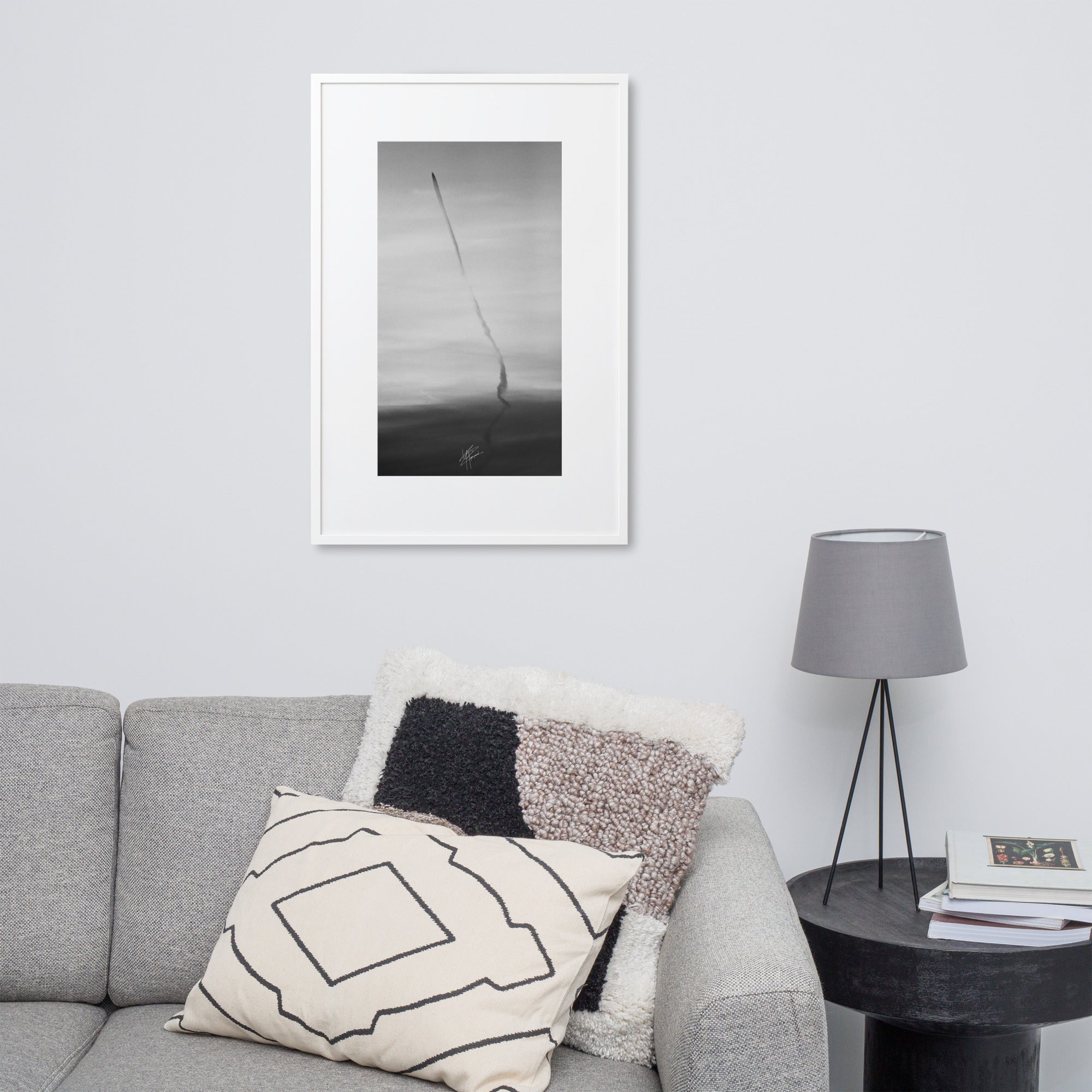 Photographie en noir et blanc du ciel avec des traces d'avions formant une longue ligne noire, encadrée d'un cadre en bois d'ayous blanc.